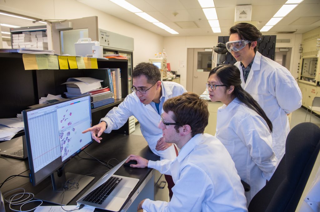 A group of scientists in a laboratory gather around a computer screen.