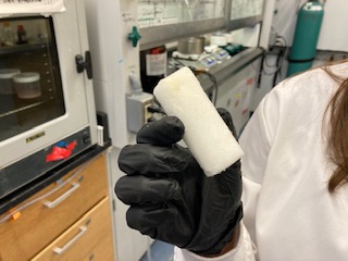 A scientist's gloved hand in a laboratory holding a piece of white material.