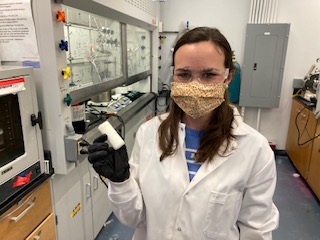 Professor Monroe wearing a lab coat in her chemical laboratory holding a sample of her smart foam.