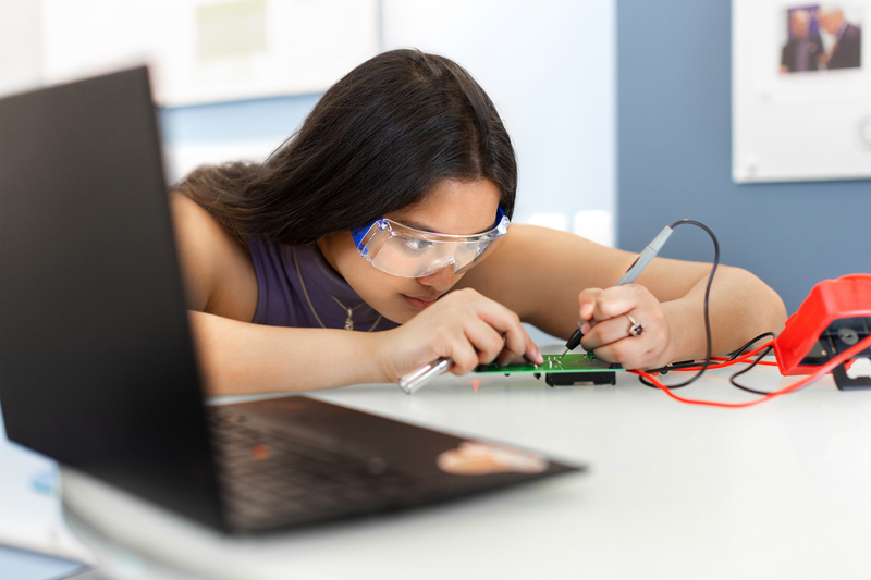 A young woman solders a circuit board