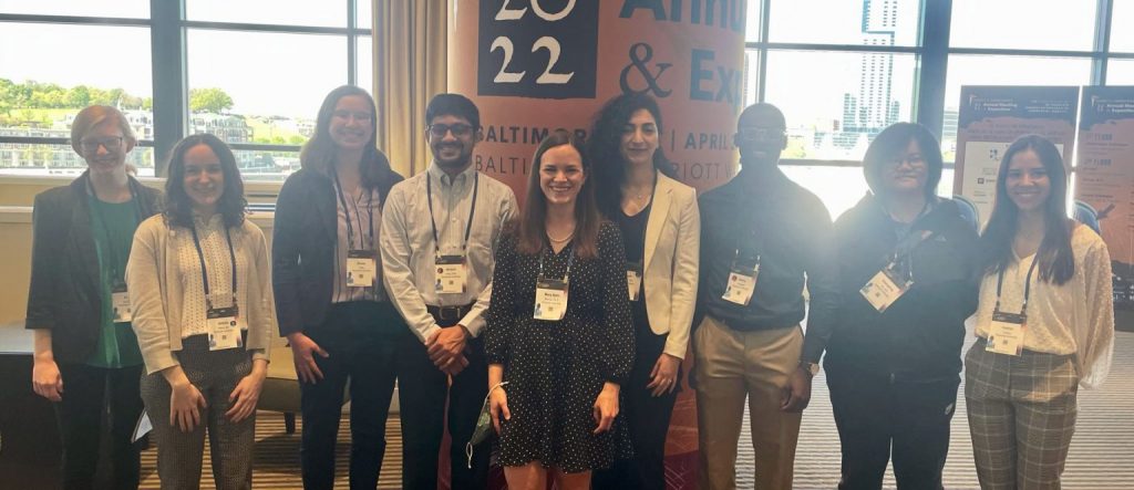 A group of 9 people smiling in front of a conference sign.