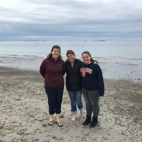 Three researchers smiling on a sandy beach under an overcast sky