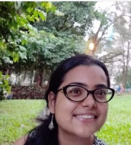 Headshot of a smiling Renita Saldanha in a green park.