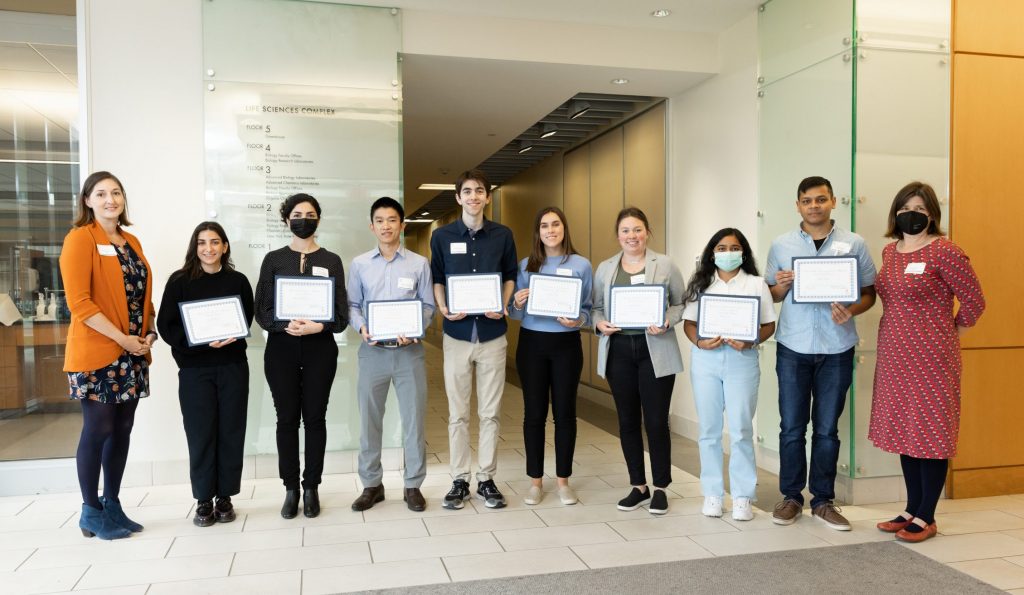 A row of graduate students holding certificates smiling for the camera