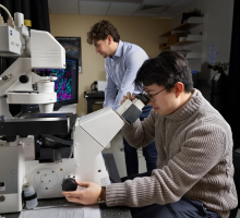 A student operates a confocal microscope in the foreground, while another student works in the background.