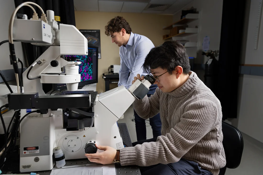 A student operates a confocal microscope in the foreground, while another student works in the background.