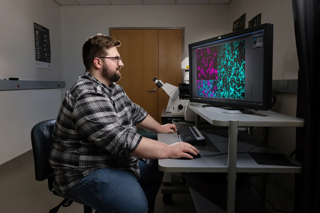 A student operates a confocal microscope in a darkened room.