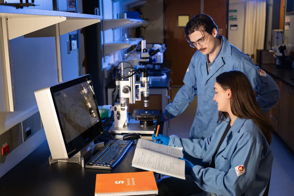 Sadie and Matty Lesko looking at notebook in front of computer in lab.